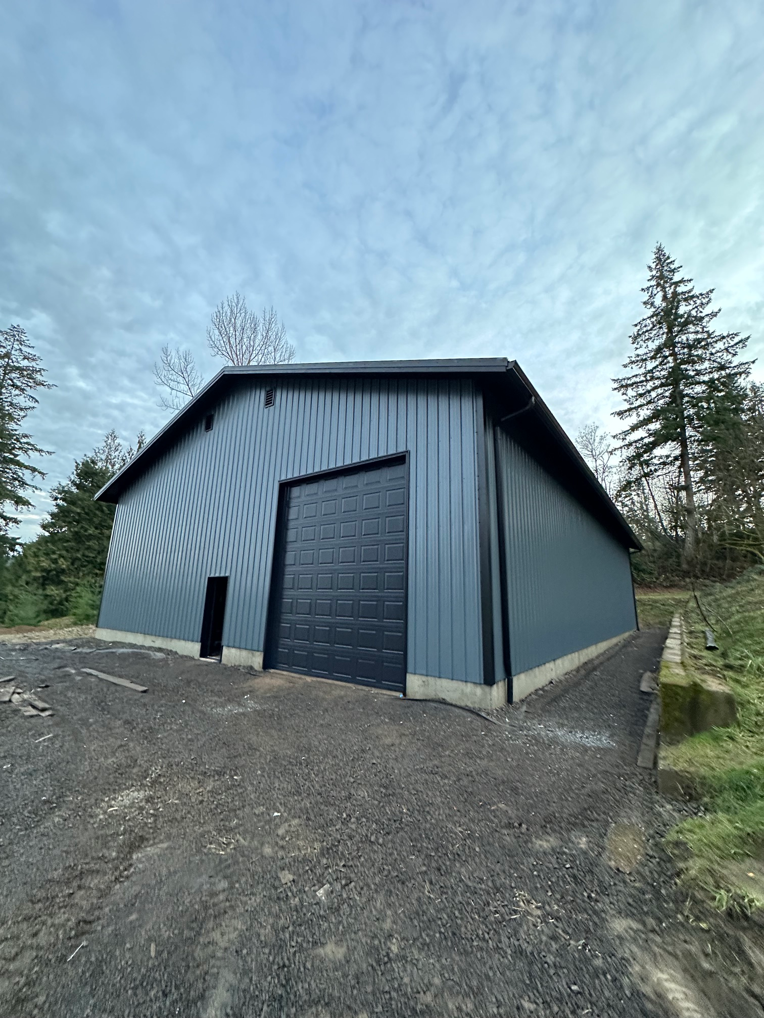 Custom detached garage and workshop with dark metal siding and a large roll-up door in the Portland, Oregon area.