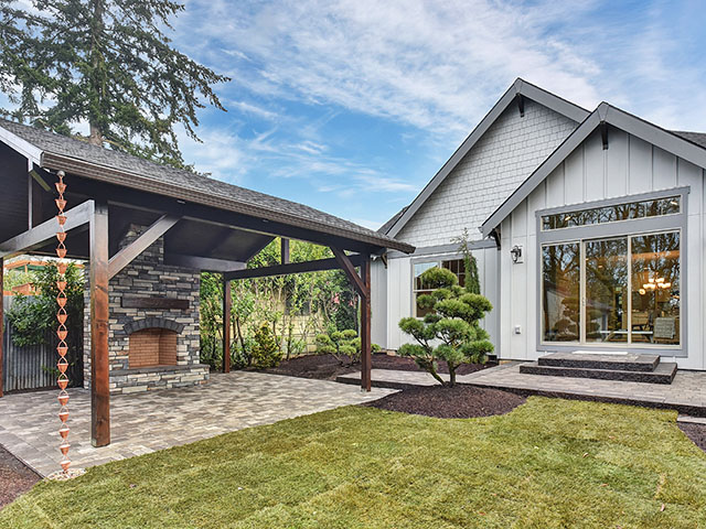 Finished covered patio connected to a custom home with landscaping and an outdoor stone fireplace.