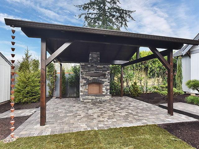 Covered outdoor living area featuring a stone fireplace and paved patio.